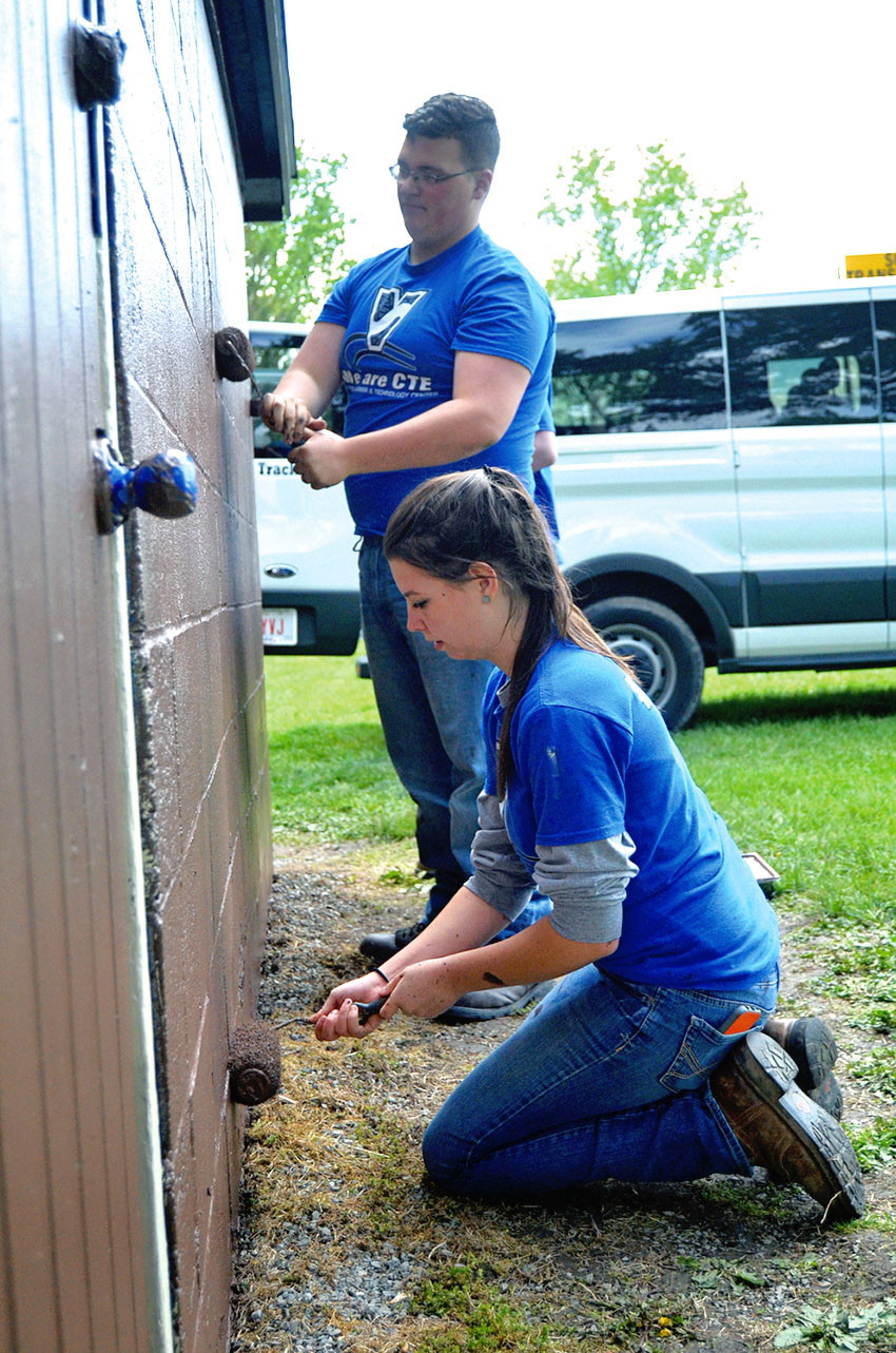 Tori Stansbery (front) and Gage Stahl roll paint on a building side.